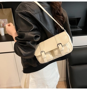 Chic cream leather shoulder bag with silver buckles styled on a black leather jacket