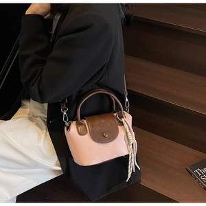 Pink and brown crossbody bag shown on a model sitting on wooden stairs in a blazer