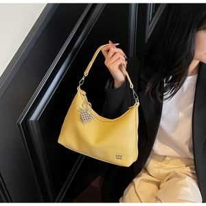 Close-up of bright yellow lychee texture leather shoulder bag with silver heart charm