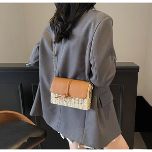 Crossbody straw bag with brown leather flap and gold chain shown on a model's back
