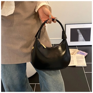 Dettaglio di una borsa hobo nera lucida con cerniera dorata e manico dal design unico