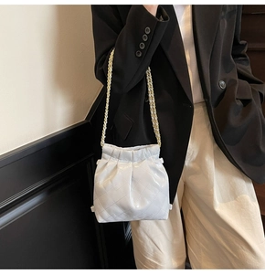 Détail d'un sac seau matelassé blanc avec chaîne dorée et finition brillante sur l'épaule