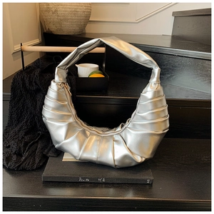 Close-up of metallic silver ruched crescent bag with integrated wide handle on dark steps