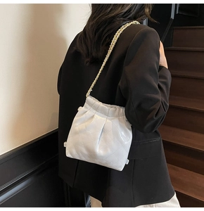 Détail d'un sac seau matelassé blanc avec chaîne dorée porté sur un blazer noir chic