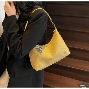 Detail of yellow lychee leather bag with silver grape pendant on model over black blazer