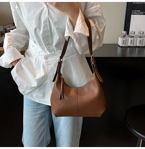 Detail of adjustable leather shoulder strap and golden metal buckle on brown crescent bag