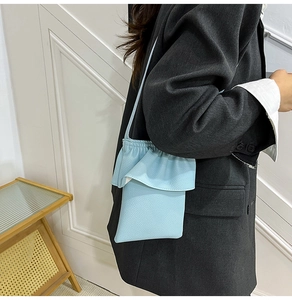 Détail du sac seau bleu clair avec bord volanté et texture litchi porté à l'épaule