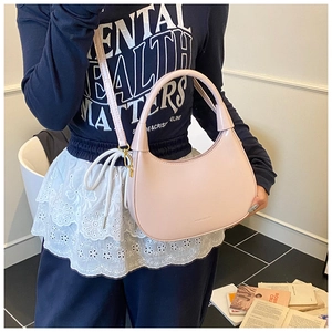 Detail of light pink half-moon shoulder bag with gold hardware worn by a model