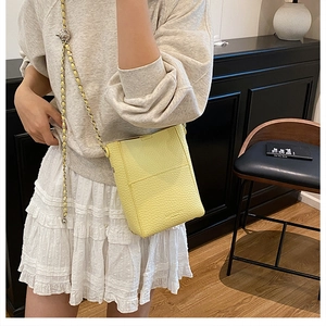 Detailed view of pale yellow pebble leather bag with gold chain and metal ball charm