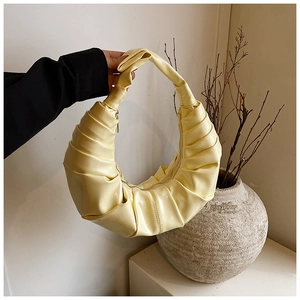 Detail of light yellow ruched crescent handbag with pleated faux leather texture and zipper