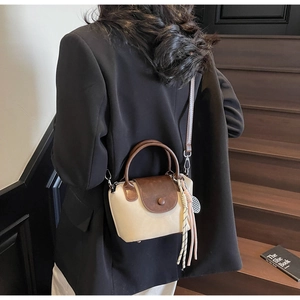 Detail of a beige and brown crossbody bag with woven charm on a wooden staircase