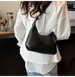 Side view of a black crescent shoulder bag with adjustable strap in a cafe setting
