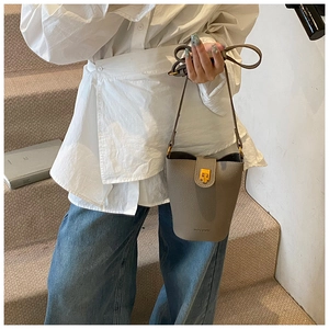 Close-up of elephant gray pebble leather bucket bag with gold metal clasp on stairs
