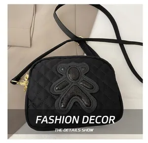 Detail showing the quilted black crossbody bag with a sequined bear patch and gold hardware