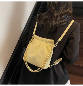 Detailed view of yellow quilted drawstring bucket bag with gold chain strap on shoulder