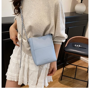 Close-up of light blue pebble leather crossbody bucket bag with woven chain strap on a model
