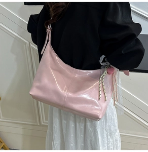 Close-up of pink glossy hobo bag with lace charms and heart pendants on shoulder strap