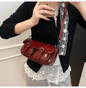 Detail view of dark red glossy patent leather crossbody bag with dual buckled front pockets