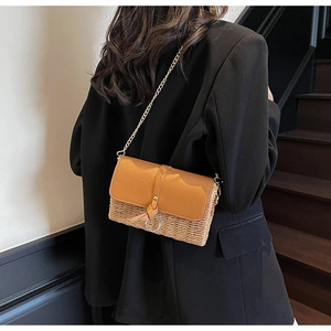 Detail of straw woven crossbody bag with brown leather flap and gold chain on model