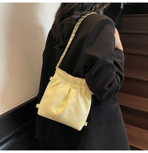Détail du sac à bandoulière matelassé beige avec chaîne porté sur un blazer noir