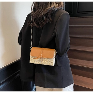 Chic straw and brown leather crossbody bag with chain strap worn by a model