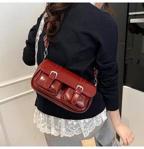 Detail of burgundy glossy leather shoulder bag with silver buckles on dual front pockets