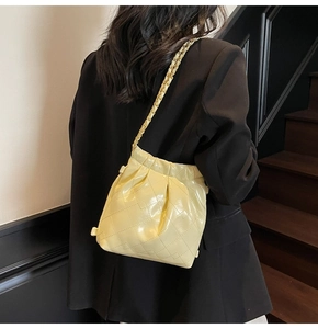 Gros plan d'un sac seau matelassé jaune clair avec bandoulière chaîne sur un blazer noir