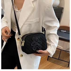 Detail of black quilted crossbody bag with sequined bear patch and gold zippers