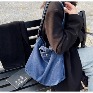 Detail of a large denim tote bag with side button pockets and wide shoulder strap