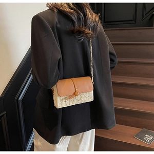 Detailed view of woven straw crossbody bag with brown leather flap and gold chain