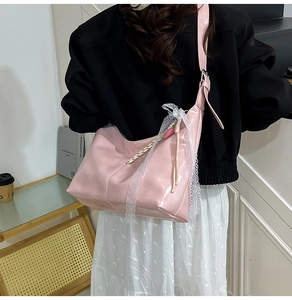 Pink glossy leather shoulder bag with lace trim and bow detail in a lifestyle setting