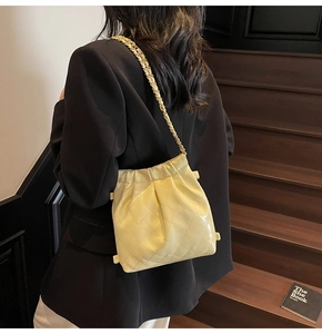 Détail du sac seau matelassé jaune clair avec chaîne dorée porté par un modèle
