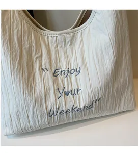 Detail of soft wrinkled off-white canvas tote with blue Enjoy Your Weekend embroidery