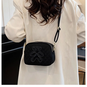 Close-up of quilted black crossbody bag with sequined bear patch and dual zippers