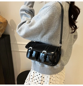 Detail of glossy black patent leather shoulder bag with silver buckles and dual pockets