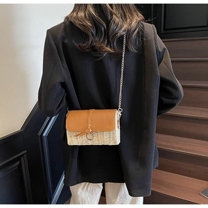 Detail of woven straw crossbody bag with brown leather flap and gold ring closure