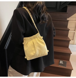 Detail of a beige quilted bucket bag with gold chain strap on a model at stairs