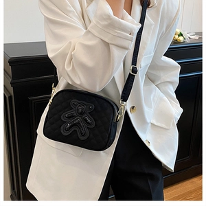 Detail of black quilted crossbody bag with sequined bear and golden hardware accents