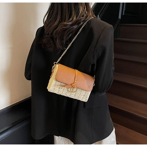 Detail of straw beach bag with brown leather flap and golden chain strap on a model