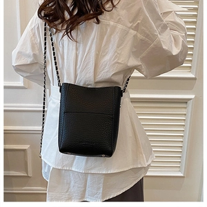Close-up of black litchi leather bucket bag featuring gold-tone chain strap details