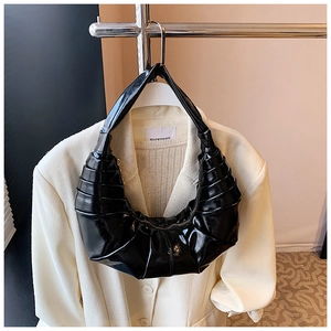 Detail of black patent leather crescent bag featuring textured pleats and minimalist design