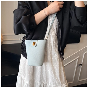 Detail of light blue bucket bag with gold clasp and fine leather texture worn by model