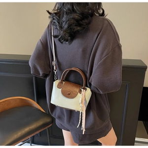 Detail view of two-tone crossbody bag on model featuring brown leather handle and fringe