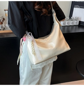 Detail of a white patent leather hobo bag with lace trim and heart charm pendant