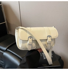 Detail of cream white leather crossbody bag featuring dual front buckle pockets and silver hardware