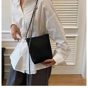 Detail shot of black pebbled leather bucket bag with silver chain strap on a model