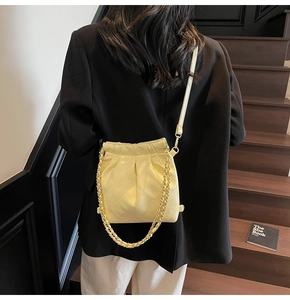 Détail du sac seau matelassé jaune clair avec chaîne dorée porté par un mannequin stylé
