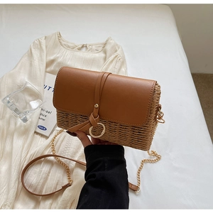 Detail of a straw crossbody bag with brown leather flap and golden ring buckle