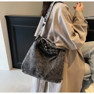 Detailed side view of washed denim tote bag with wide straps on model in trench coat