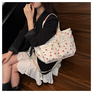 Détail d'un sac fourre-tout blanc à motif cerise avec plusieurs poches zippées fonctionnelles